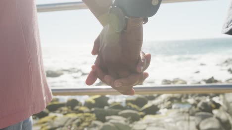 Close-up-of-senior-african-american-couple-holding-hands-on-promenade-by-the-sea,-slow-motion