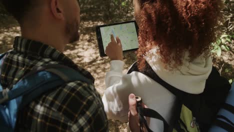 Happy-african-american-couple-wearing-backpack,-using-tablet-in-forest,-slow-motion