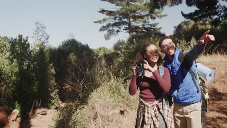 Happy-african-american-couple-hiking-and-wearing-backpacks,-taking-pictures-in-forest,-slow-motion