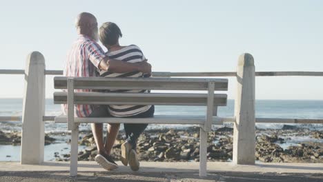 Glückliches-älteres-Afroamerikanisches-Paar-Sitzt-Auf-Einer-Bank-An-Der-Promenade-Am-Meer,-Zeitlupe