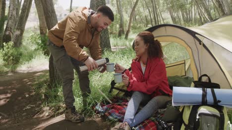 Happy-african-american-couple-camping,-drinking-coffee-in-forest,-slow-motion