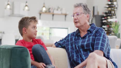 Caucasian-grandfather-and-grandson-sitting-on-sofa-and-talking,-slow-motion