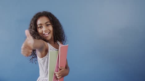 Portrait-of-happy-african-american-girl-holding-books-on-blue-background,-copy-space,-slow-motion
