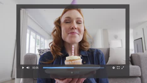 Animation-of-video-screen-over-caucasian-woman-holding-cupcake-and-blowing-candle