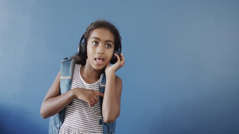 Fröhliches-Afroamerikanisches-Mädchen-Mit-Kopfhörern-Auf-Blauem-Hintergrund,-Kopierraum,-Zeitlupe