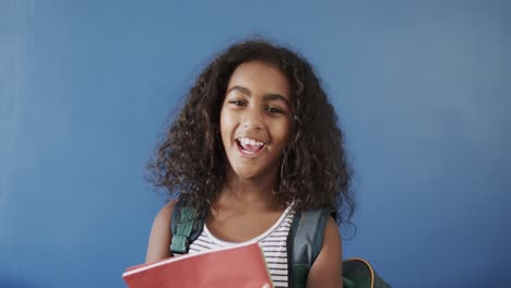 Portrait-of-happy-african-american-girl-holding-books-on-blue-background,-slow-motion