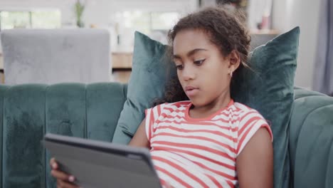 Happy-african-american-girl-sitting-on-sofa,-using-tablet,-slow-motion