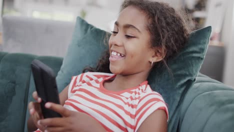 Happy-african-american-girl-sitting-on-sofa,-using-smartphone,-slow-motion