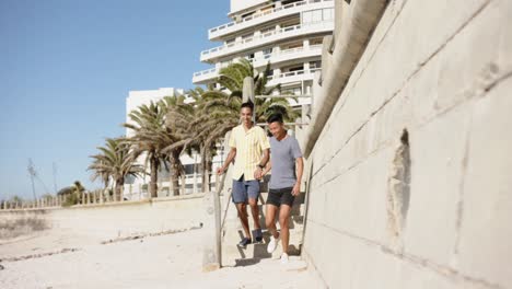 Happy-diverse-gay-male-couple-walking-and-holding-hands-at-beach,-slow-motion