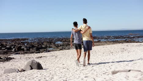 Happy-diverse-gay-male-couple-walking-and-embracing-at-beach,-slow-motion