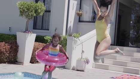 Happy-african-american-mother-and-daughter-jumping-into-swimming-pool,-slow-motion