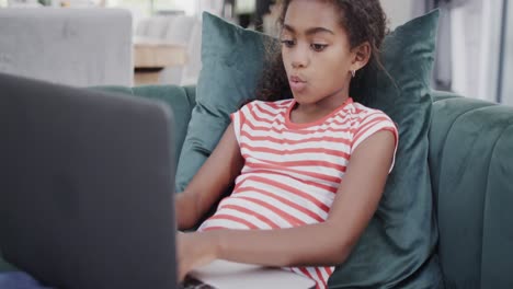 Happy-african-american-girl-sitting-on-sofa,-using-laptop,-slow-motion