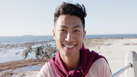 Portrait-of-happy-biracial-man-looking-at-camera-at-promenade-by-the-sea,-slow-motion