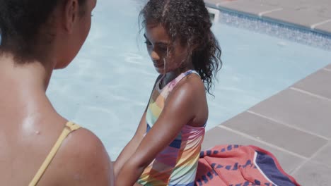 Happy-african-american-mother-and-daughter-applying-sunscreen-by-swimming-pool,-slow-motion