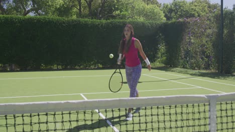Happy-biracial-woman-playing-tennis-in-garden-on-sunny-day