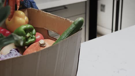 Hands-of-senior-caucasian-woman-unpacking-fresh-vegetables-from-box-in-kitchen,-slow-motion