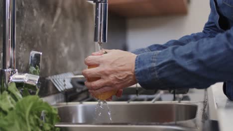 Midsection-of-senior-caucasian-woman-washing-yellow-pepper-in-kitchen-sink,-slow-motion