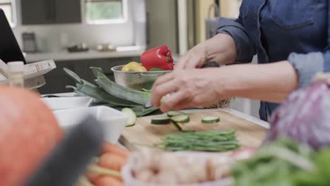 Midsection-of-senior-caucasian-woman-chopping-vegetables-in-kitchen,-slow-motion