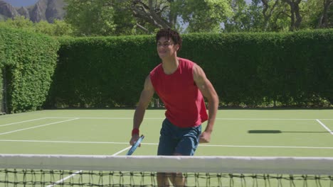 Happy-biracial-man-playing-tennis-in-garden-on-sunny-day