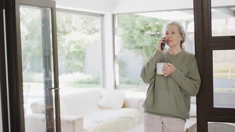 Happy-senior-caucasian-woman-talking-on-smartphone-and-drinking-tea,-slow-motion