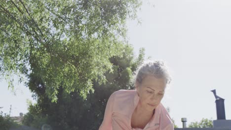 Happy-senior-caucasian-woman-doing-yoga,-stretching-and-meditating-in-sunny-garden,-slow-motion