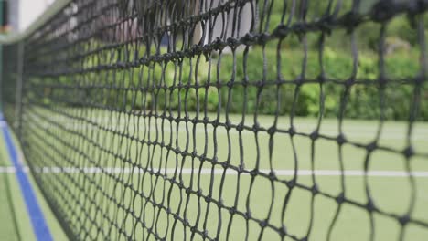 Close-up-of-tennis-net-and-ball-on-tennis-court-in-garden-on-sunny-day