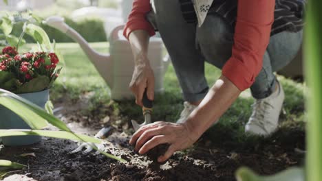 Midsection-of-senior-caucasian-woman-digging-earth-with-trowel-in-garden,-slow-motion