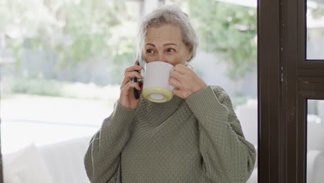 Glückliche-ältere-Kaukasische-Frau,-Die-Auf-Dem-Smartphone-Spricht-Und-Tee-Trinkt,-Zeitlupe