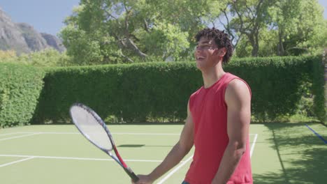 Happy-biracial-man-with-tennis-racket-laughing-in-garden-on-sunny-day