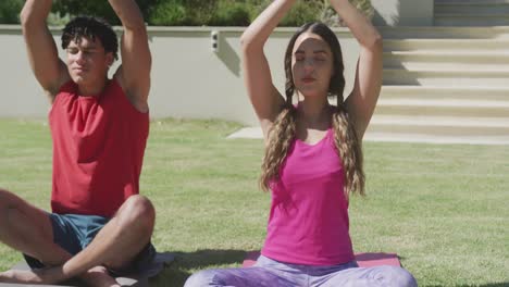 Focused-biracial-couple-practicing-yoga-and-meditating-in-garden-on-sunny-day