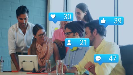 Animation-of-social-media-icons-over-diverse-colleagues-discussing-together-at-office