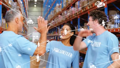 Animation-of-network-of-icons-over-diverse-volunteers-high-fiving-each-other-at-warehouse