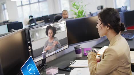 Diverse-businesswomen-on-computer-video-call-with-data-processing-on-laptop-in-office