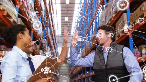 Animation-of-network-of-icons-over-team-of-diverse-supervisors-high-fiving-each-other-at-warehouse