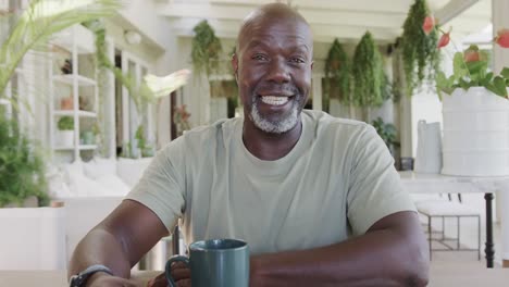 Porträt-Eines-Glücklichen-älteren-Afroamerikanischen-Mannes-Mit-Kaffee,-Der-Einen-Videoanruf-In-Zeitlupe-Führt