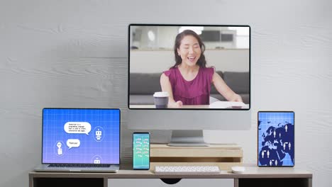Asian-businesswoman-on-video-call-and-electronic-devices-with-data-processing-on-screens