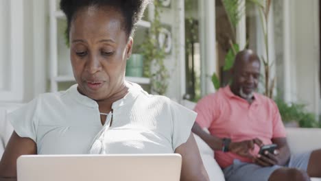 Happy-senior-african-american-couple-using-laptop-and-smartphone-in-slow-motion