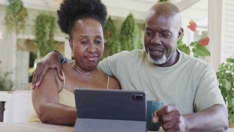 Glückliches-älteres-Afroamerikanisches-Paar,-Das-Kaffee-Trinkt-Und-In-Zeitlupe-Ein-Tablet-Benutzt
