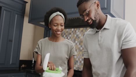 Glückliches-Afroamerikanisches-Paar,-Das-In-Zeitlupe-Lebensmittelabfälle-In-Der-Küche-Wegwirft