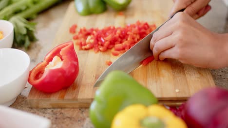 Close-up-of-biracial-woman-wearing-apron-and-cutting-vegetables-in-kitchen-in-slow-motion