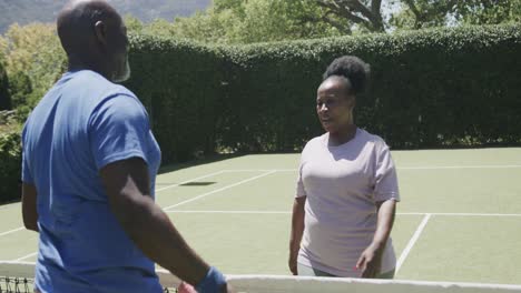 Glückliches-älteres-Afroamerikanisches-Paar,-Das-In-Zeitlupe-Tennis-Spielt-Und-Sich-Auf-Dem-Tennisplatz-Umarmt