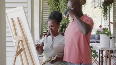Happy-senior-african-american-couple-painting-and-drinking-coffee-in-slow-motion