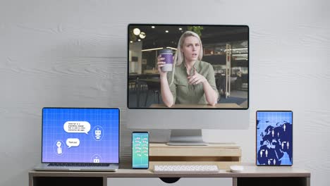 Caucasian-businesswoman-on-video-call-and-electronic-devices-with-data-processing-on-screens