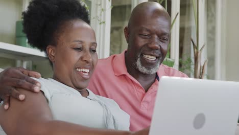 Glückliches-älteres-Afroamerikanisches-Paar,-Das-Laptop-In-Zeitlupe-Umarmt-Und-Benutzt