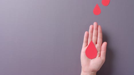 Hand-of-caucasian-woman-holding-blood-drop-on-grey-background-with-copy-space,-slow-motion