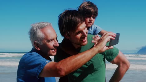 Animation-of-camera-icons-over-caucasian-man-with-son-and-grandson-using-smartphone