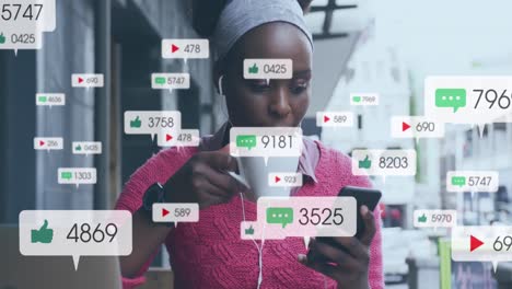 Animation-Von-Social-Media-Symbolen-Mit-Zahlen-über-Einer-Afroamerikanischen-Frau,-Die-Ihr-Smartphone-Nutzt