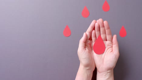 Hands-of-caucasian-woman-holding-blood-drop,-on-grey-background-with-copy-space,-slow-motion