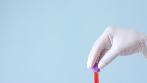 Hand-wearing-medical-glove-holding-blood-sample-on-blue-background-with-copy-space,-slow-motion