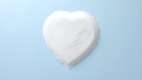 Close-up-of-sugar-in-heart-shape-on-blue-background-with-copy-space,-slow-motion